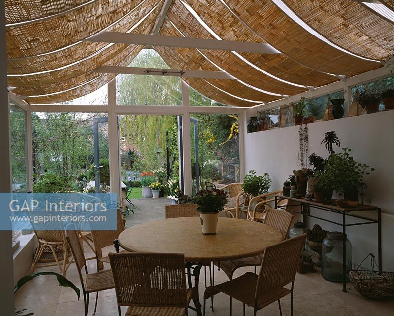 View of country conservatory with roof blinds and dining table and view to garden