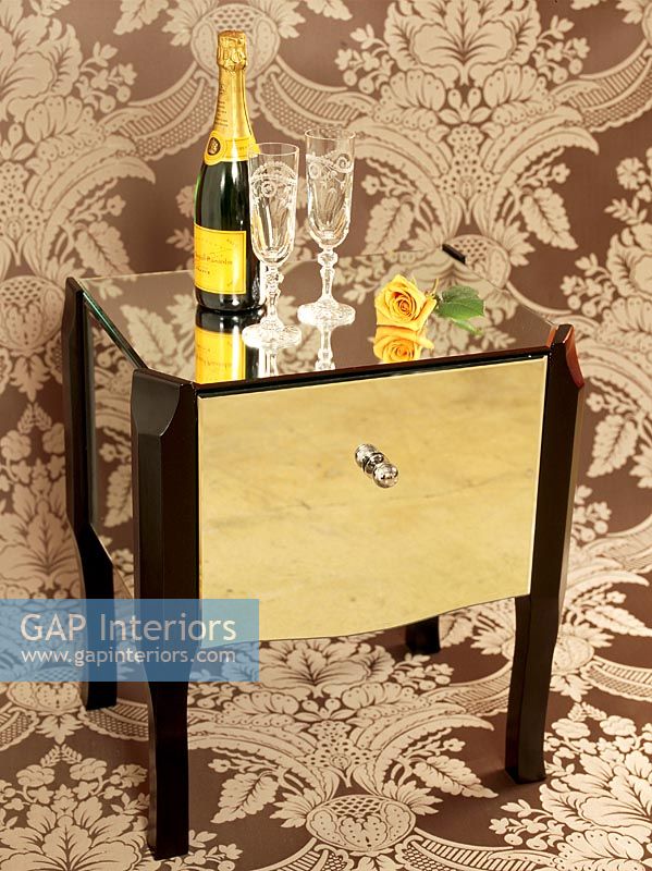Champagne and glasses on a table in front of an ornate wallpaper