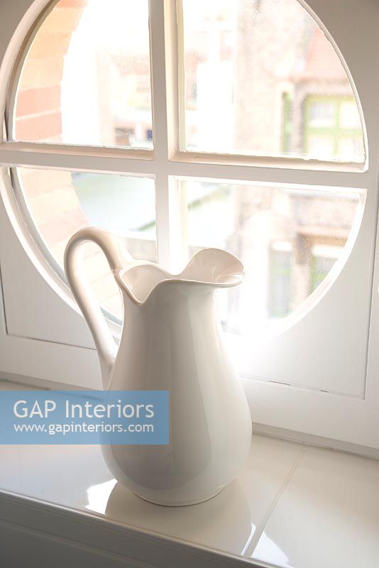 White jug on windowsill by round window 