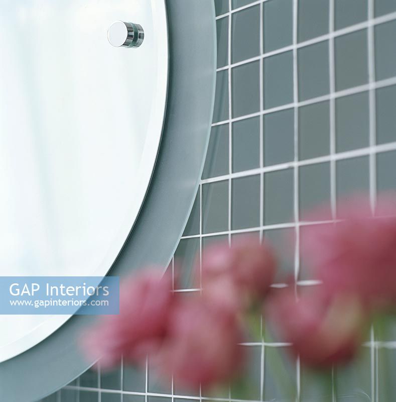 Close-up of a round bathroom mirror with out of focus flowers
