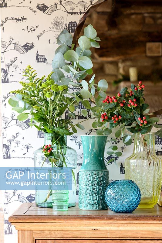 Arrangements of foliage and berries in colourful vases