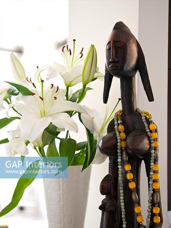 White Lilies in retro vase next to tribal sculpture