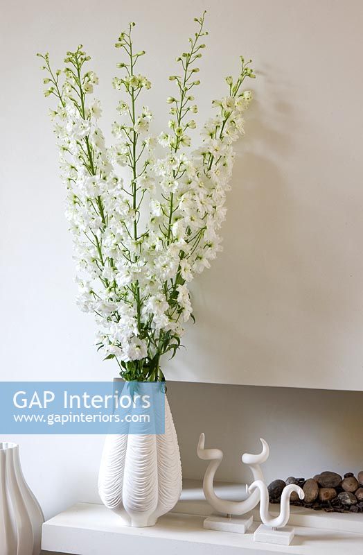 White Larkspur flowers in vase by limestone fireplace