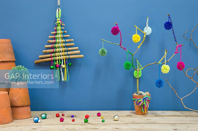 A colourful christmas tree made with sticks, coloured wool and miniature baubles against a blue backdrop