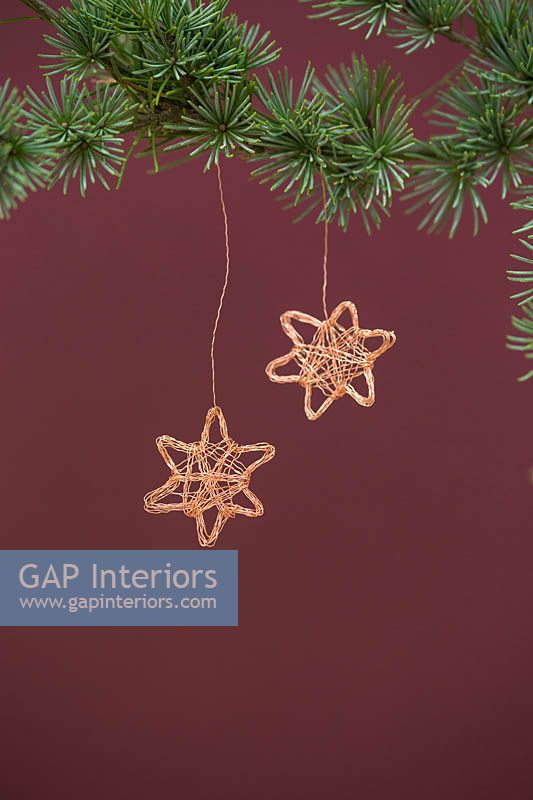 Making copper wire stars - finished decorations hanging from a conifer branch