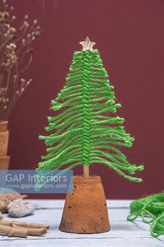 Christmas tree made from green wool mounted in an upturned terracotta pot, against a burgundy background 