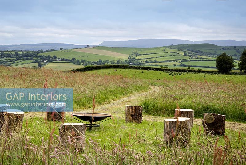 Circle of log stools around fire bowl with extensive countryside views beyond 