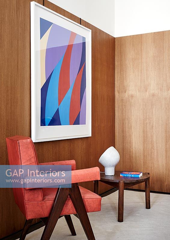 Red leather armchair, wooden walls and colourful artwork 