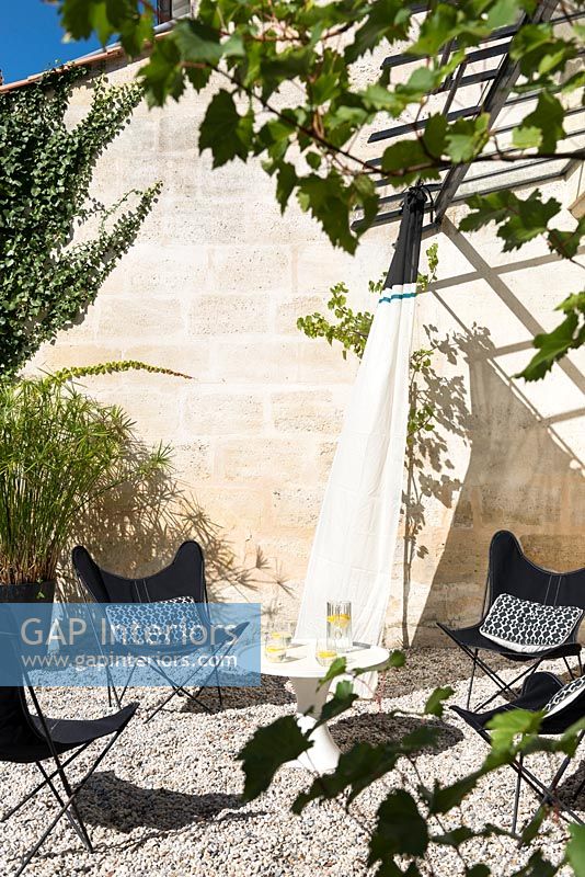 Black and white furniture on gravel terrace with grapevine growing on pergola