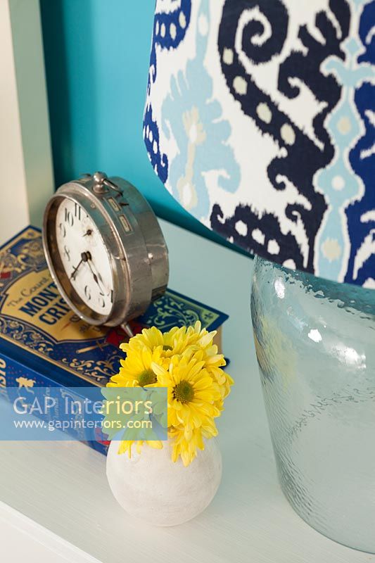 Small vase of yellow flowers and alarm clock on bedside table 