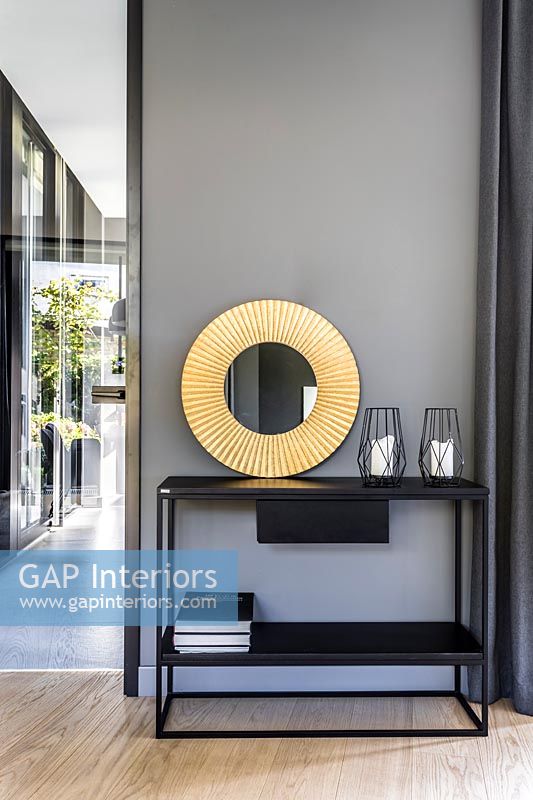Console table with circular gold mirror against grey painted wall 