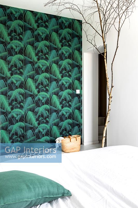 Green wallpapered feature wall and bare tree branch ornament in modern bedroom
