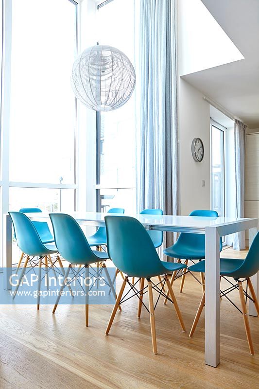 Modern white dining room with turquoise chairs and wooden floor 