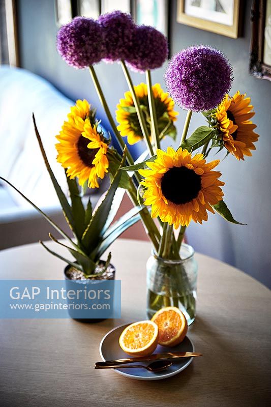 Sunflowers and alliums in vases on small dining table 