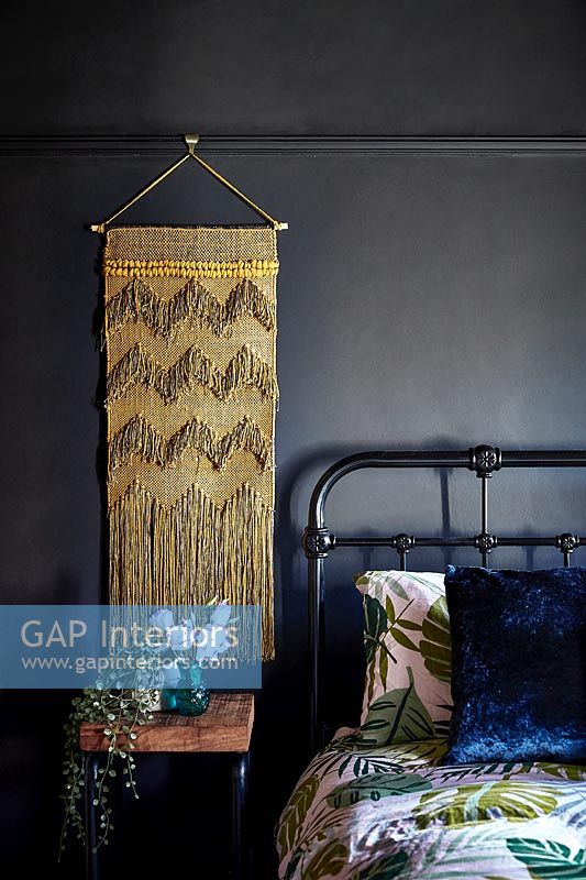 Golden wall hanging in modern bedroom with vintage iron bed frame 