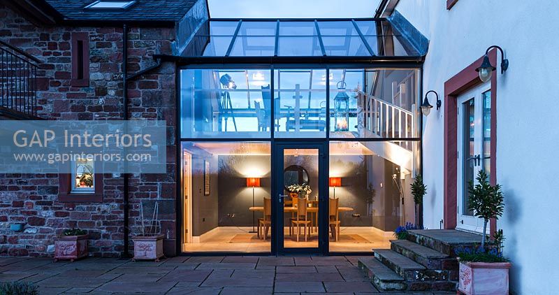Country house exterior with modern glazed joining room illuminated in evening 
