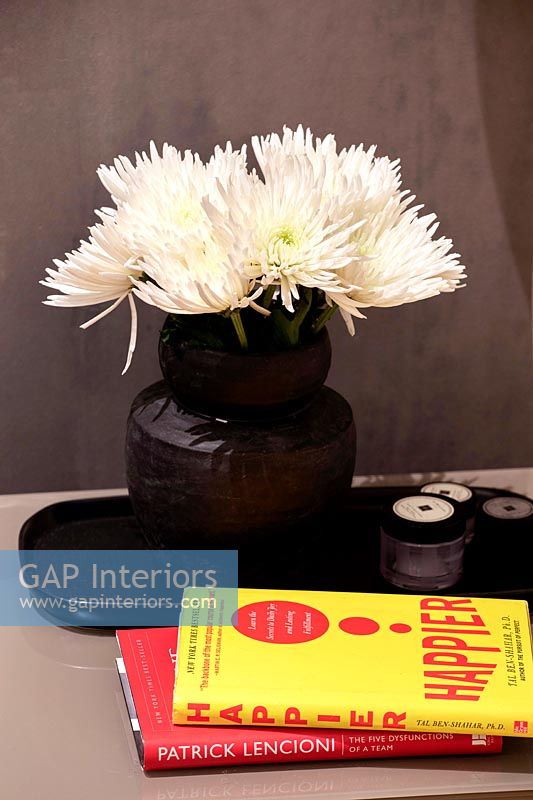 Black vase with white cut flowers on bedside table with reading material 