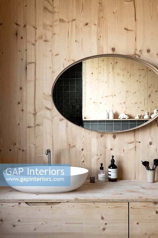 Large oval mirror above sink in wooden bathroom 