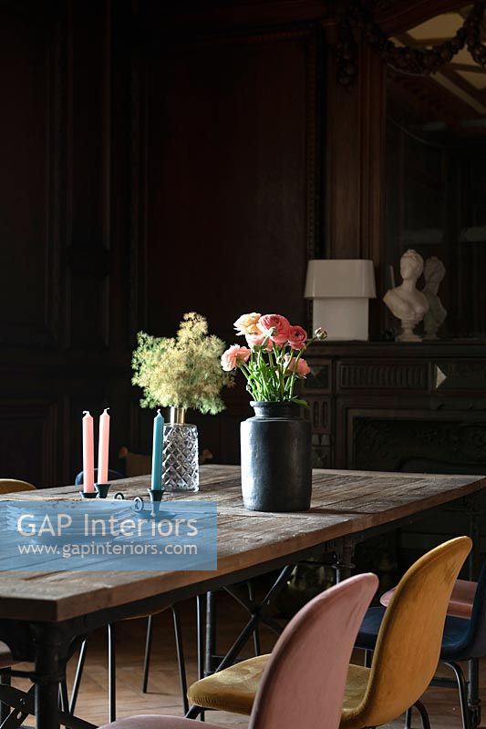 Flowers on large wooden dining table in dark dining room 
