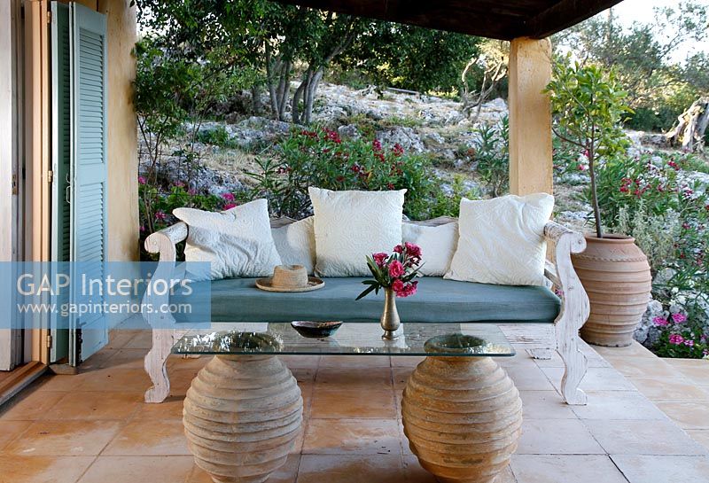 Ornate wooden sofa on covered terrace with glass and clay urn table
