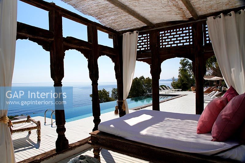 Decorative pergola with large bed on outdoor terrace with pool and sea views 