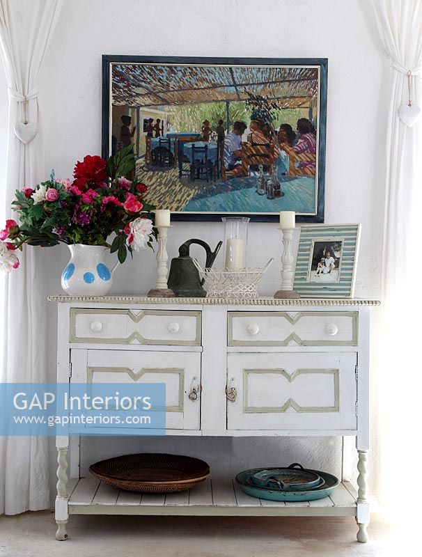 White wooden sideboard with large painting behind on wall 