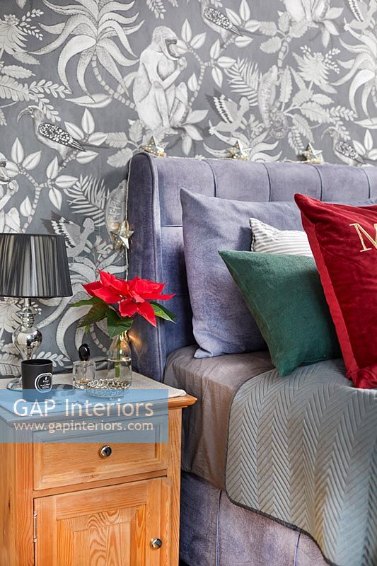 Poinsettia flower on bedside table with Christmas themed cushion on bed