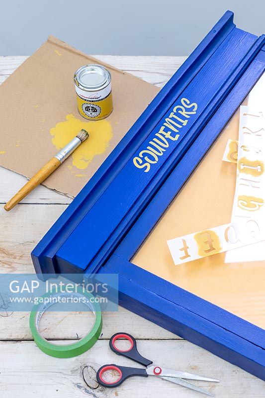 Adding stencil lettering to blue painted notice board frame 
