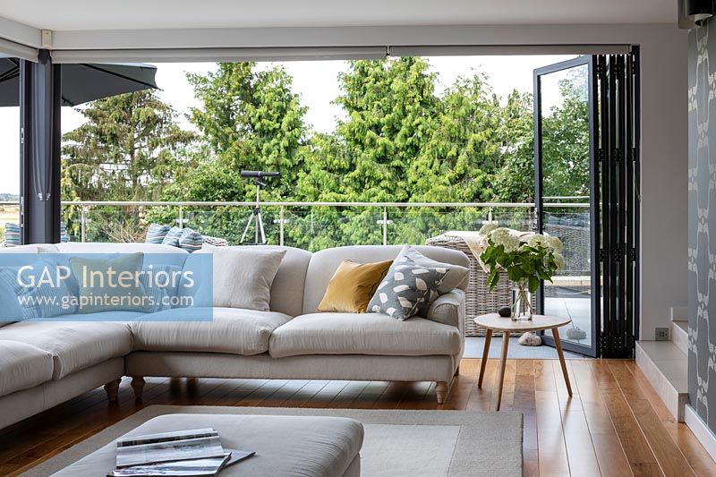 Modern corner sofa in living room with open bi-fold doors to balcony 