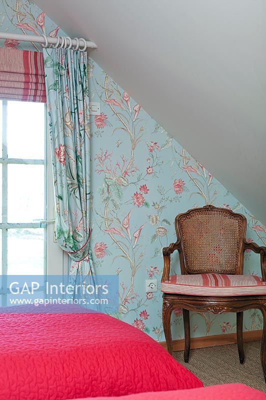Wooden armchair against colourful floral wallpapered wall in bedroom 