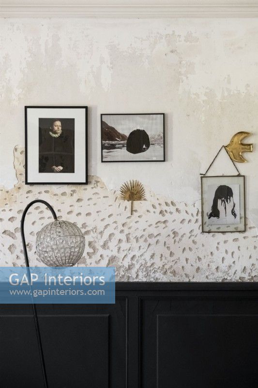 Display of paintings and photographs on bare plaster wall