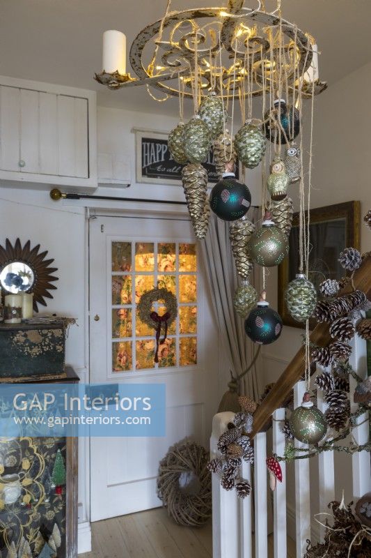 Christmas baubles hanging from ornate candelabra in hallway of country cottage