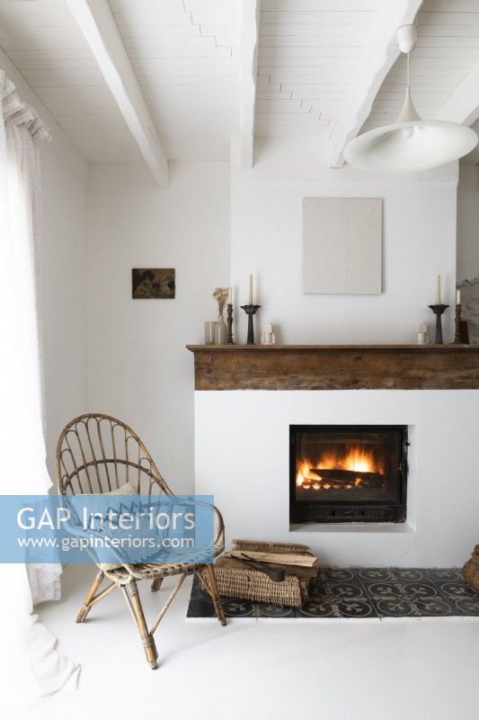 Wicker chair next to lit fireplace in white country living room