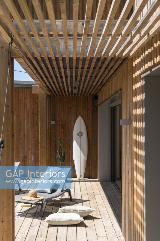 Surfboard against wall and recliners on decking - summer