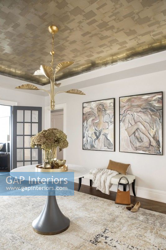 Modern foyer entrance decorated with pedestal table, artwork and gold metal leaf wallpaper on ceiling.