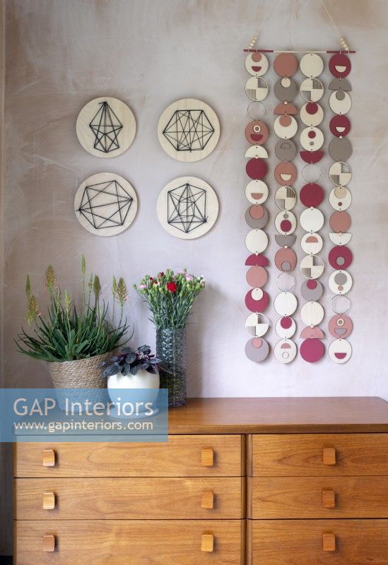 Colourful wall hanging on bare plaster wall above wooden sideboard