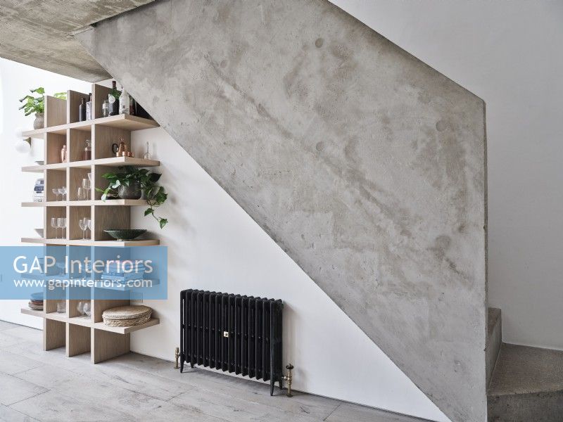 Black radiator and contemporary shelving under concrete stairway