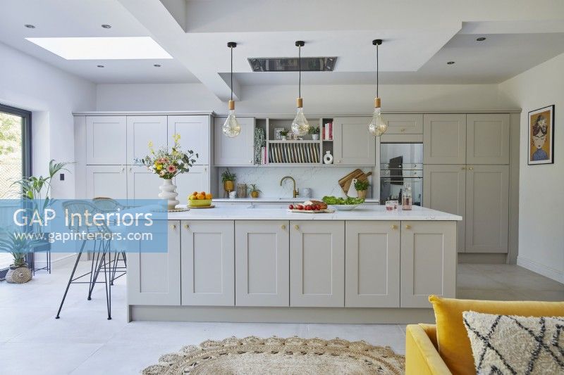 Modern kitchen with grey shaker-style cabinets. Large island with pendant lights and a bar.