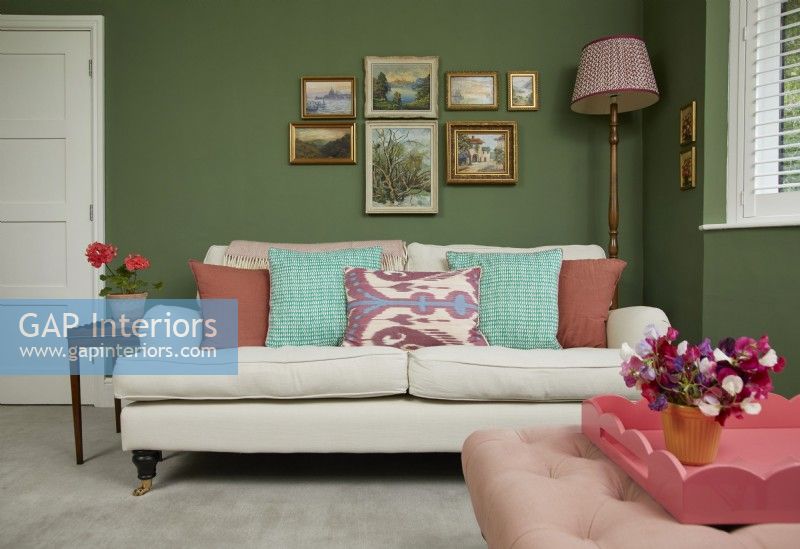 Living room with a cream sofa, vintage oil paintings and a green painted wall.