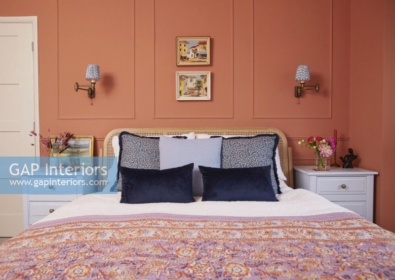 Bedroom with terracotta painted panelling, fitted wall lights and vintage oil paintings.