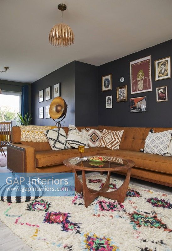 Living room with a brown leather sofa, vintage coffee table, a gallery of framed prints and dark blue painted walls.
