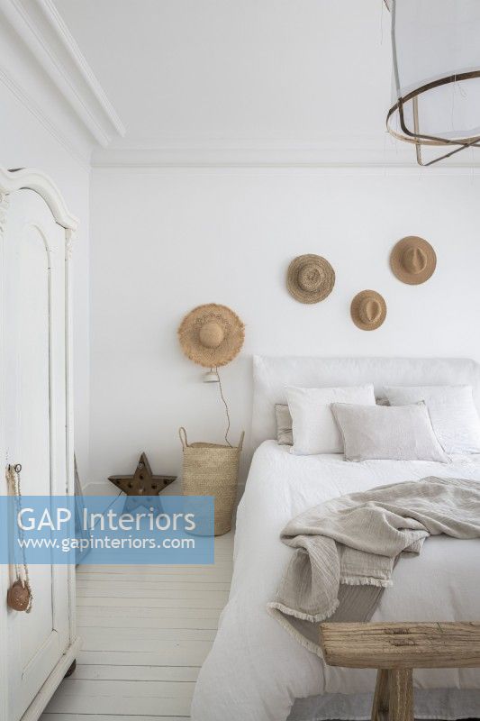 Display of straw hats on white country bedroom wall