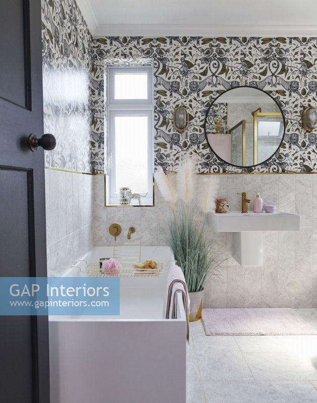 Bathroom with patterned wallpaper, round mirror and gold tap details.