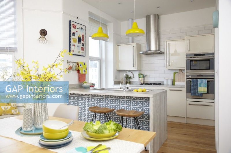 Open plan kitchen-diner with breakfast bar and yellow pendant lights.