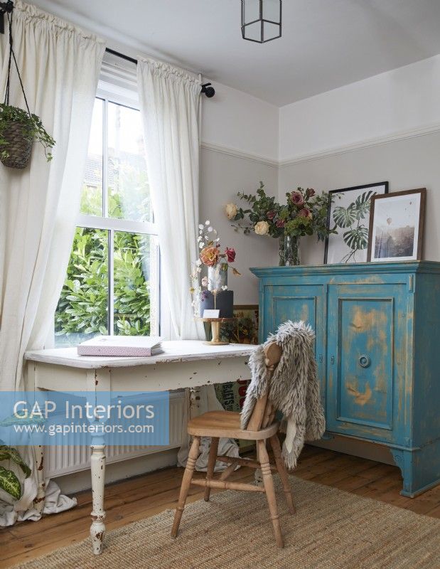 Home office space with desk, shabby chic turquoise cupboard and artwork.