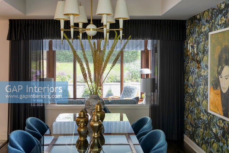 Dining room with glass table and blue chairs and floral patterned wallpaper.