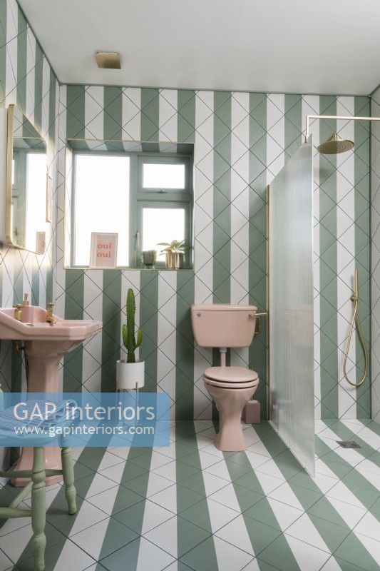 Green and white stripey tiled bathroom with pink sanitary ware