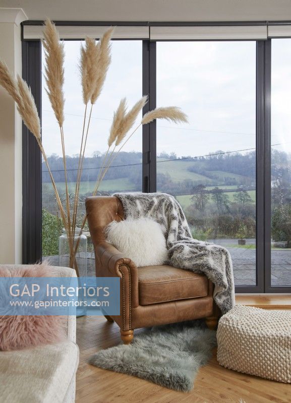 Leather armchair with pampas grass and a countryside view through bifold doors.
