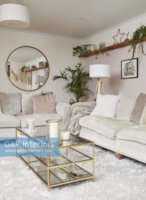Living room with neutral sofas, a gold coffee table, open shelving and a round mirror.