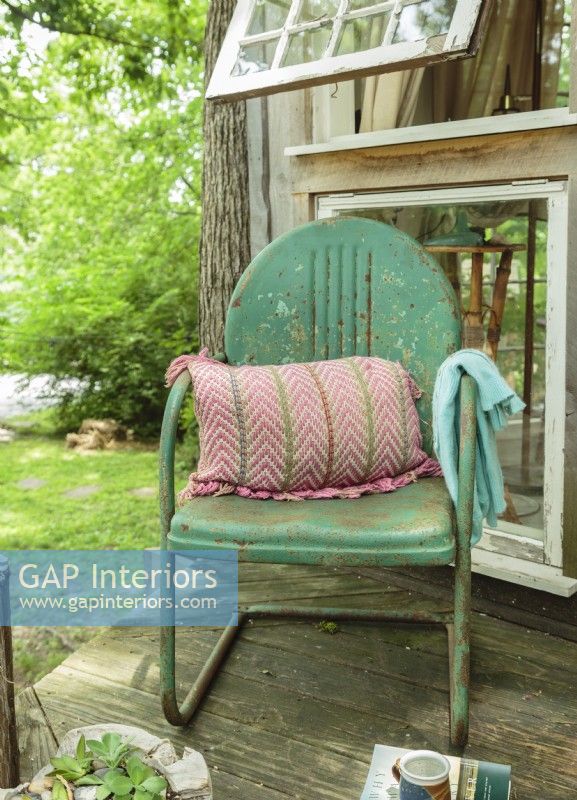 A weathered vintage metal garden chair is made comfortable with a pillow and a throw for wildlife watching